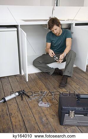 Mid adult man repairing a faucet in the kitchen View Large Photo Image Stock Image - Mid adult man repairing a faucet in the kitchen. Fotosearch
