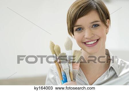 Stock Image - Portrait of a young woman holding paintbrushes. Fotosearch