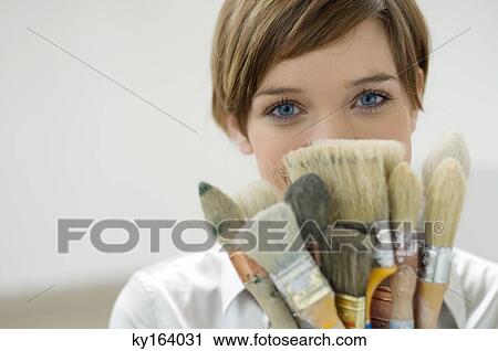 Portrait of a young woman holding paintbrushes in front of her face View Large Photo Image Stock Image - Portrait of a young woman holding paintbrushes in front of her face. Fotosearch