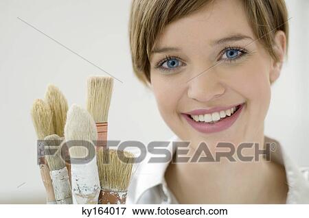 Stock Photo - Portrait of a young woman holding paintbrushes. Fotosearch