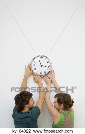 Rear view of a mid adult man and a young woman mounting a clock on the wall View Large Photo Image Stock Image - Rear view of a mid adult man and a young woman mounting a clock on the wall. Fotosearch