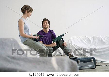 Stock Photograph - Young couple sitting in a room holding drills. Fotosearch