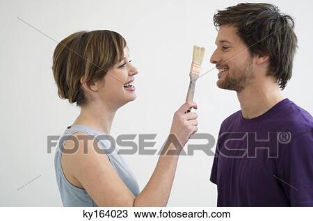 Young woman holding a paintbrush in front of a mid adult man's face View Large Photo Image Stock Image - Young woman holding a paintbrush in front of a mid adult man's face. Fotosearch