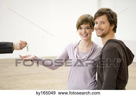 Stock Photo - Close-up of a real estate agent's hand handing over the keys to a couple. Fotosearch