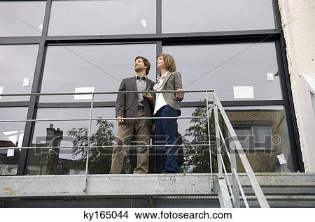 Picture - Low angle view of a mid adult man and a young woman standing at a balcony. Fotosearch
