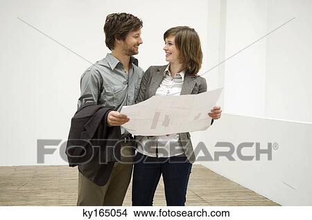 Mid adult man and a young woman holding a blueprint and looking at each other View Large Photo Image Picture - Mid adult man and a young woman holding a blueprint and looking at each other. Fotosearch