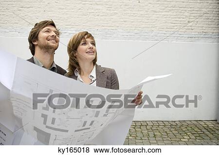 Stock Photo - Mid adult man and a young woman holding a blueprint. Fotosearch