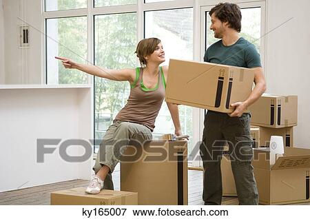 Stock Photo - Mid adult man holding a cardboard box and a young woman pointing away. Fotosearch