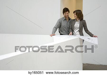 Mid adult man looking at a blueprint and smiling with a young woman standing beside him View Large Photo Image Stock Image - Mid adult man looking at a blueprint and smiling with a young woman standing beside him. Fotosearch