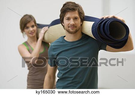 Stock Image - Portrait of a couple carrying a carpet. Fotosearch