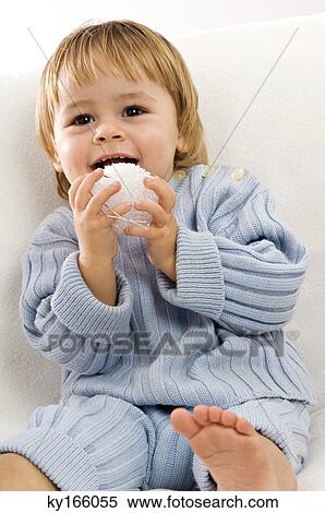 Stock Photography - Close-up of a baby boy sitting on a couch and playing with a toy. Fotosearch