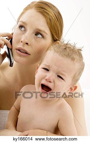 Close-up of a young woman talking on a mobile phone and holding a crying baby boy View Large Photo Image Picture - Close-up of a young woman talking on a mobile phone and holding a crying baby boy. Fotosearch