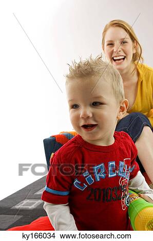 Portrait of a young woman sitting on a couch and smiling with her son standing in front of her View Large Photo Image Picture - Portrait of a young woman sitting on a couch and smiling with her son standing in front of her. Fotosearch