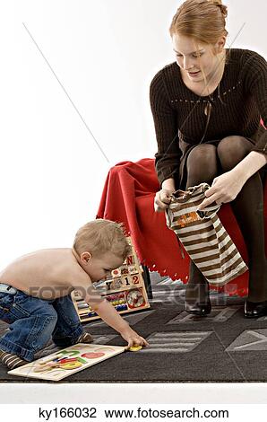 Young woman holding a baby t-shirt with her son playing in front of her View Large Photo Image Stock Image - Young woman holding a baby t-shirt with her son playing in front of her. Fotosearch