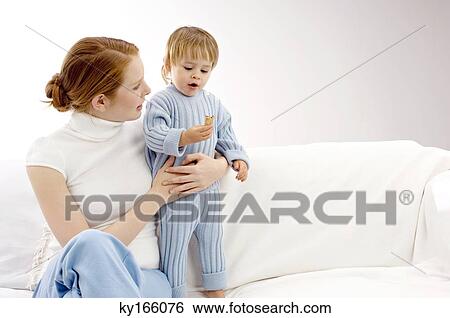 Young woman sitting on a couch with her son holding a biscuit View Large Photo Image Stock Photograph - Young woman sitting on a couch with her son holding a biscuit. Fotosearch