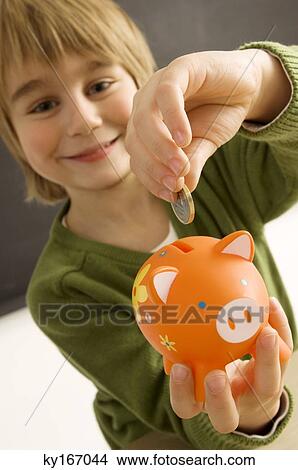 Picture - Boy putting a coin into a piggy bank. Fotosearch