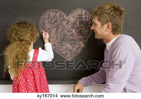 Girl drawing on a blackboard with her father watching her View Large Photo Image Picture - Girl drawing on a blackboard with her father watching her. Fotosearch
