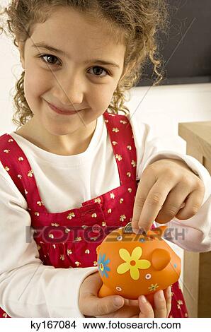 Picture - Girl putting a coin into a piggy bank. Fotosearch
