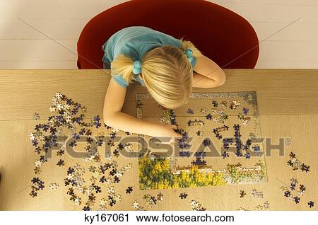 Stock Image - High angle view of a girl playing a jigsaw puzzle. Fotosearch