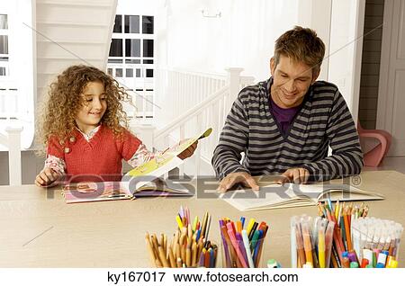 Stock Photo - Mid adult man sitting with his daughter and reading books. Fotosearch