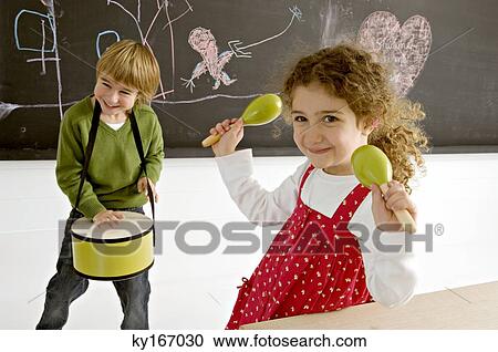 Stock Image - Portrait of a girl holding maracas and her brother playing drum. Fotosearch