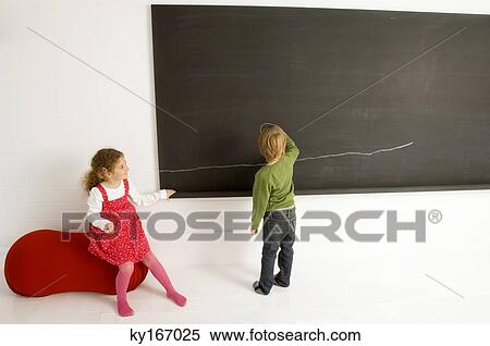 Rear view of a boy drawing on a blackboard with his sister sitting beside him View Large Photo Image Stock Photography - Rear view of a boy drawing on a blackboard with his sister sitting beside him. Fotosearch