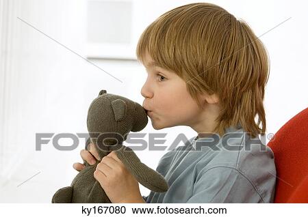 Stock Image - Side profile of a boy kissing a teddy bear. Fotosearch