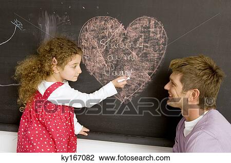 Side profile of a girl drawing on the blackboard with her father watching her View Large Photo Image Stock Image - Side profile of a girl drawing on the blackboard with her father watching her. Fotosearch