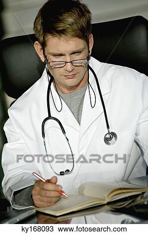 Close-up of a male doctor sitting at a desk and reading a notebook View Large Photo Image Stock Image - Close-up of a male doctor sitting at a desk and reading a notebook. Fotosearch