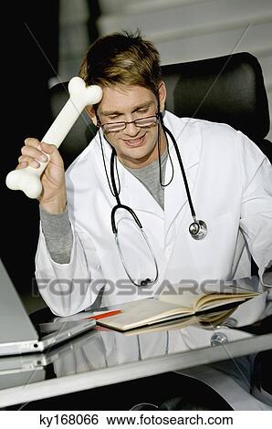 Close-up of a male doctor sitting at a desk and holding a bone View Large Photo Image Stock Photograph - Close-up of a male doctor sitting at a desk and holding a bone. Fotosearch