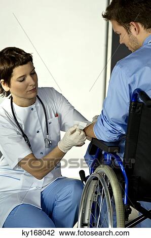 Stock Image - Female doctor applying adhesive bandage on a patient's hand. Fotosearch