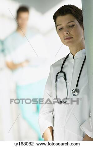 Stock Image - Female doctor leaning against a column and looking serious. Fotosearch