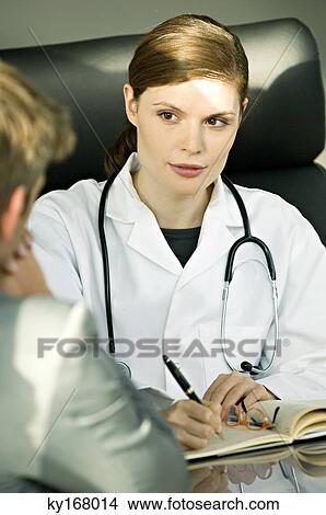 Female doctor sitting at a desk and talking with a patient View Large Photo Image Picture - Female doctor sitting at a desk and talking with a patient. Fotosearch