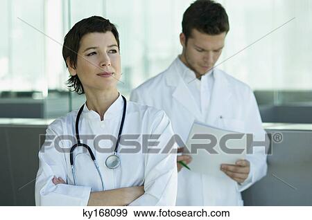 Female doctor standing with a male doctor holding medical records behind her View Large Photo Image Stock Photo - Female doctor standing with a male doctor holding medical records behind her. Fotosearch