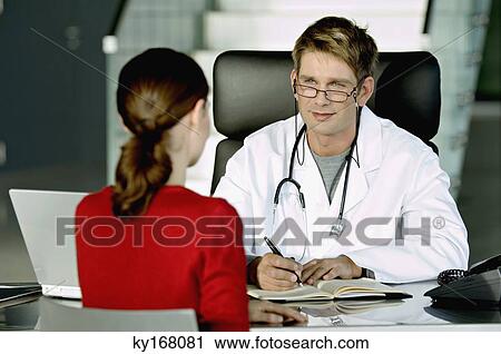 Stock Image - Male doctor discussing with a female patient in his office. Fotosearch
