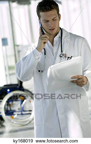 Stock Photo - Male doctor reading a medical record and talking on a mobile phone. Fotosearch