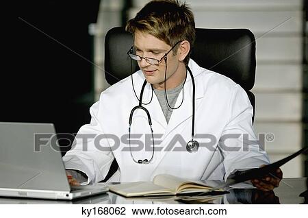Stock Image - Male doctor working on a laptop in his office. Fotosearch
