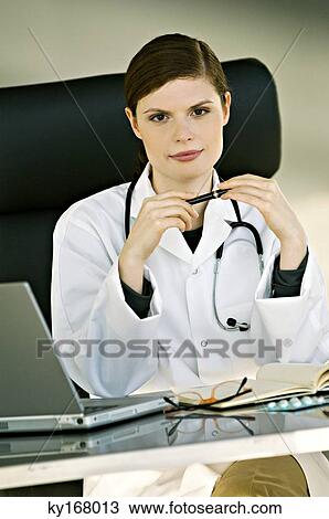 Stock Image - Portrait of a female doctor sitting at a desk in her office. Fotosearch
