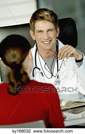 Stock Image - Portrait of a male doctor discussing with a female patient in his office. Fotosearch