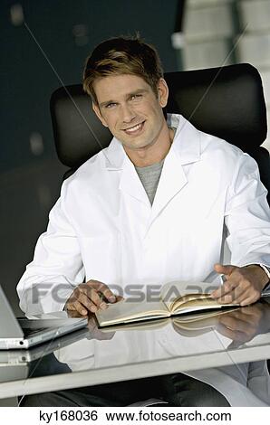 Portrait of a male doctor sitting at a desk in his office View Large Photo Image Stock Photograph - Portrait of a male doctor sitting at a desk in his office. Fotosearch