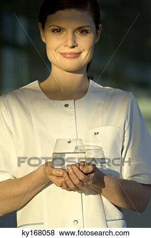 Portrait of a young woman holding a glass of water and smiling View Large Photo Image Stock Photo - Portrait of a young woman holding a glass of water and smiling. Fotosearch