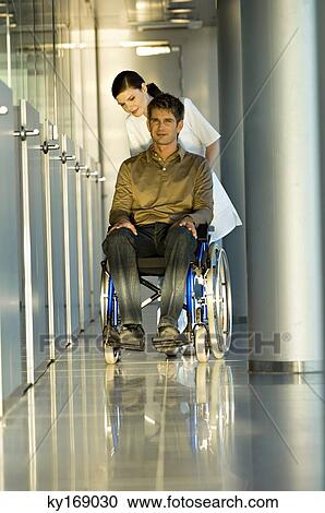 Stock Image - Female doctor pushing a male patient sitting in a wheelchair. Fotosearch