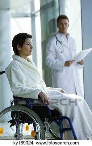Female patient sitting in a wheelchair and a male doctor standing in the background View Large Photo Image Picture - Female patient sitting in a wheelchair and a male doctor standing in the background. Fotosearch