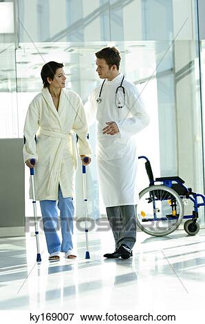 Stock Photo - Male doctor assisting a female patient in walking on crutches. Fotosearch