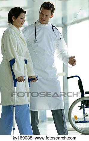 Stock Photo - Male doctor assisting a female patient in walking on crutches. Fotosearch