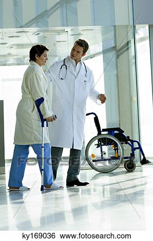 Stock Photograph - Male doctor assisting a female patient in walking on crutches. Fotosearch