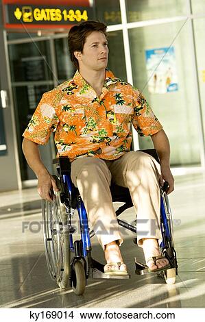 Picture - Mid adult man sitting in a wheelchair at an airport. Fotosearch