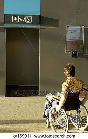 Stock Image - Rear view of a mid adult man sitting in a wheelchair. Fotosearch