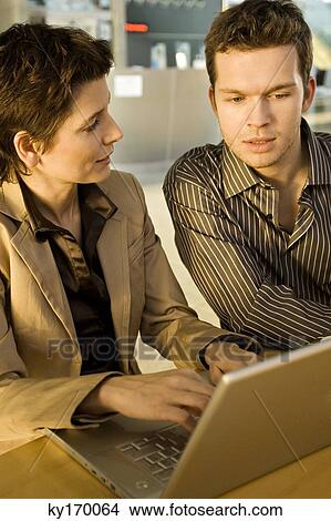 Businesswoman using a laptop with a businessman sitting beside her View Large Photo Image Picture - Businesswoman using a laptop with a businessman sitting beside her. Fotosearch