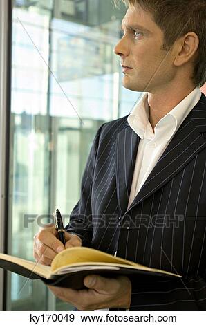Close-up of a businessman writing in a diary and looking through a window View Large Photo Image Stock Photo - Close-up of a businessman writing in a diary and looking through a window. Fotosearch